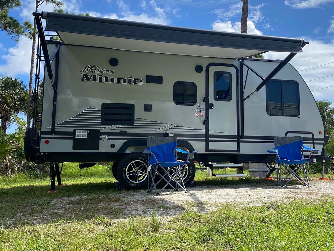 Outside view of a RV camper next to two blue lawn chairs.