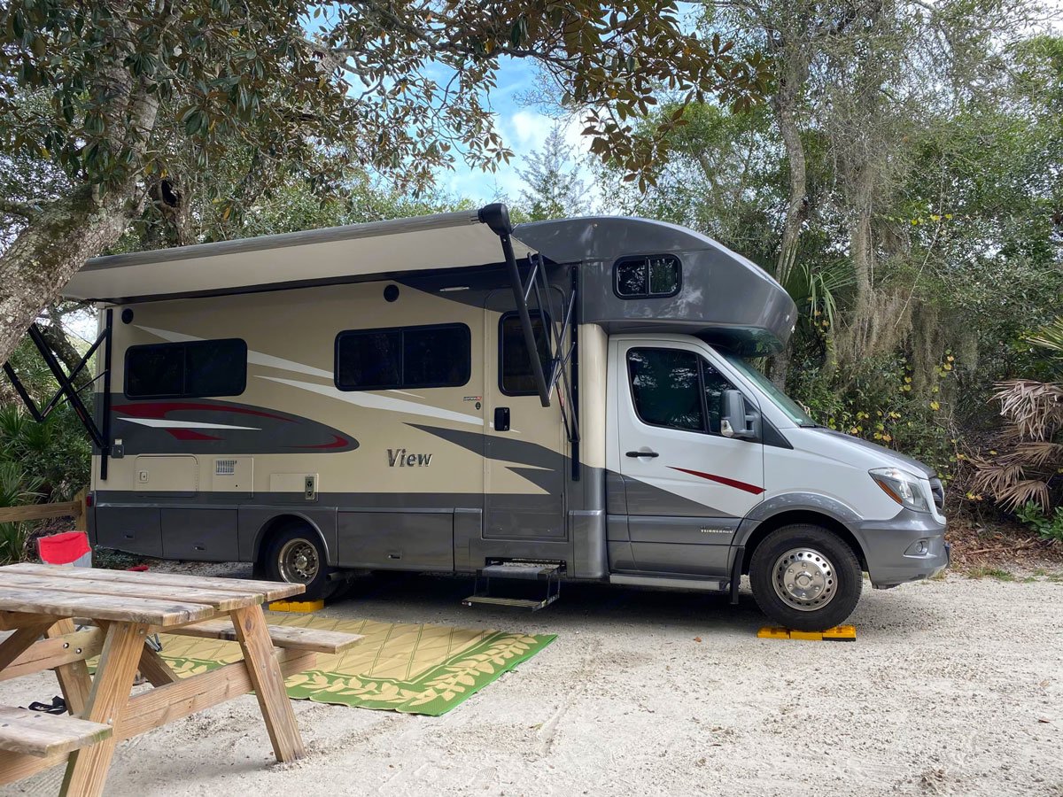 Front side view of a Motorhome parked outside next to a picnic table.